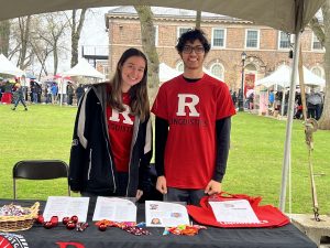 two Linguistic undergraduates stand behind a table under a tent on Voorhees Mall
