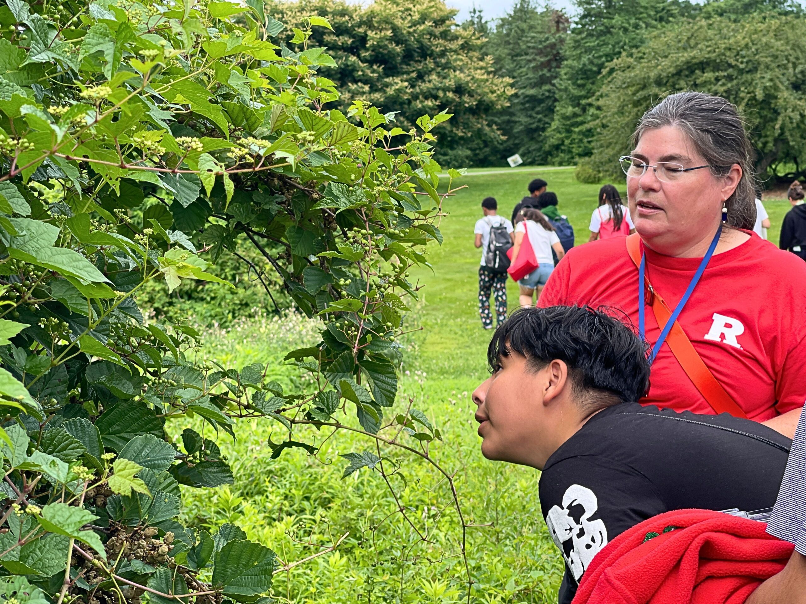 Teen boy looks at foliage as a woman looks on
