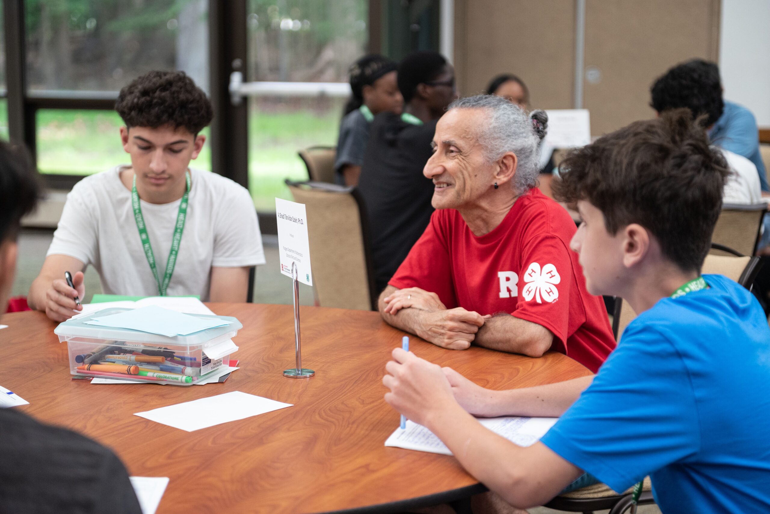 An older man sitting with two young people at a round table. He is listening intently to a person off-screen.