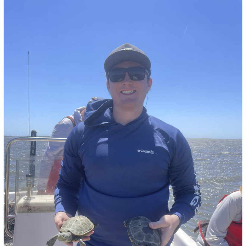 A man in shades, standing on a boat, holding a terrapin turtle