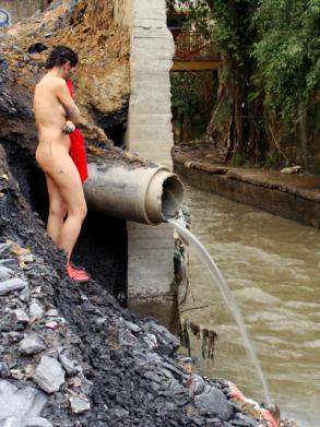 Nude women with red shoes and shirt in area of water/pollution drainage.