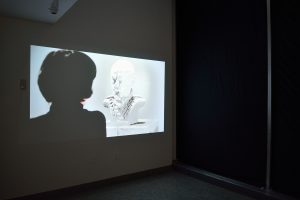 Installation view of video projection with women and white bust.