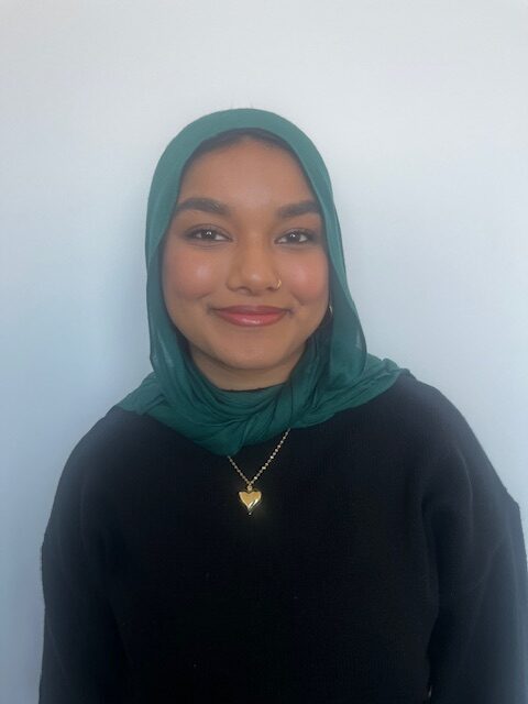 Headshot of woman in green hijab, black sweater, and gold necklace