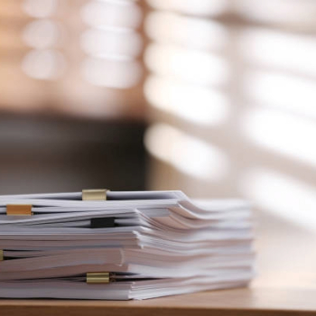 Stack of blank paper with binder clips on wooden table indoors.