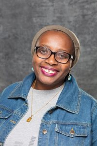 Headshot of a person in a jean jacket and light grey shirt. There is a grey marbled background.