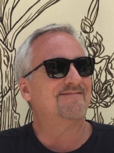 Headshot of Tim Raphael in sunglasses in front of an illustration of plants.