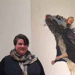 Headshot of Alison Howell standing in front of an illustration of a mouse on a wall.