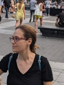 Headshot of Mary Rizzo. People in a plaza walk and sit on benches in the background.