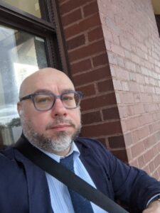 Headshot of Kyle Riismandel standing in front of a window and brick all.
