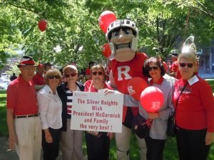 Six people posing with the Rutgers Scarlet Knight mascot in front of a banner that says, 'The Silver Knights With President McCormick and Family the Very Best'.